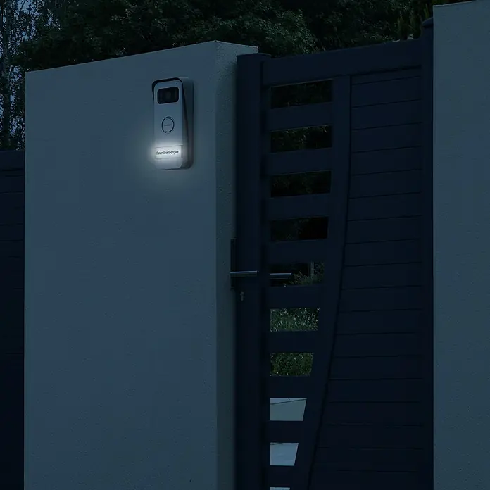 Avidsen Türklingel mit Kamera Smarte Video Türsprechanlage Elia - Weiß, Silber, 800 x 480 Pixel - Moderne Haustürklingel mit Namensschild "Familie Berger" an einer grauen Wand neben einem Tor.
