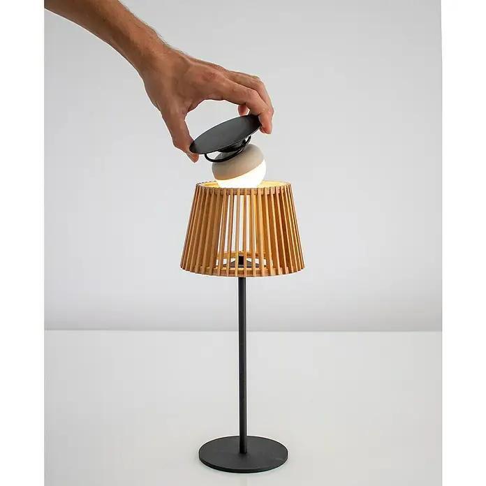 New Garden Okinawa Lámpara de sobremesa solar - 9 W, Marrón, IP54 - Una lámpara de mesa moderna con pantalla de madera y base negra, con una mano quitando la tapa de la lámpara. Diseño simple y elegante.