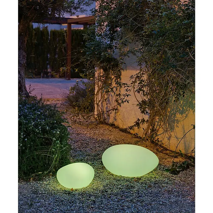Starlux Bola solar Himero 60 - Altura: 30 cm, LED - Dos luces de jardín ovaladas que brillan suavemente iluminan un camino de grava junto a una exuberante vegetación. Perfecto para un ambiente sereno.
