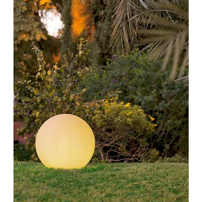 Starlux Bola solar Venus 40 - 0,5 W, 40 cm, RGB, 50 lm - Luz esférica amarilla de jardín sobre césped frente a una exuberante vegetación. Proporciona iluminación ambiental en el jardín.