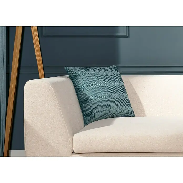 Kissen TessBlau, 45 x 45 cm, 100 % Baumwolle - Nahaufnahme eines türkisfarbenen Kissens mit plissiertem Design auf einem cremefarbenen Sofa vor einer marineblauen Wand.
