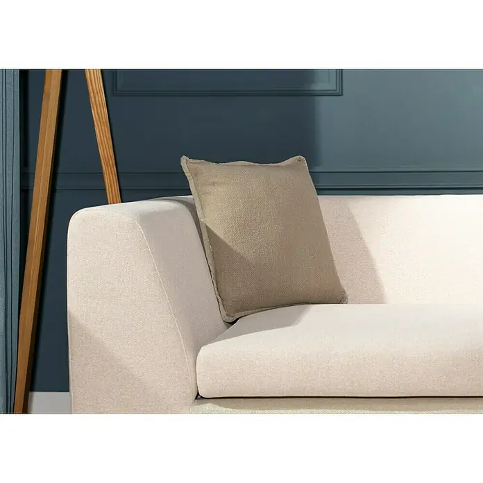Kissen Bona - Pumice Stone, 45 x 45 cm, 100 % Baumwolle - Nahaufnahme eines beigen Kissens auf einem cremefarbenen Sofa vor einer blauen Wand und einer Holzbodenlampe.