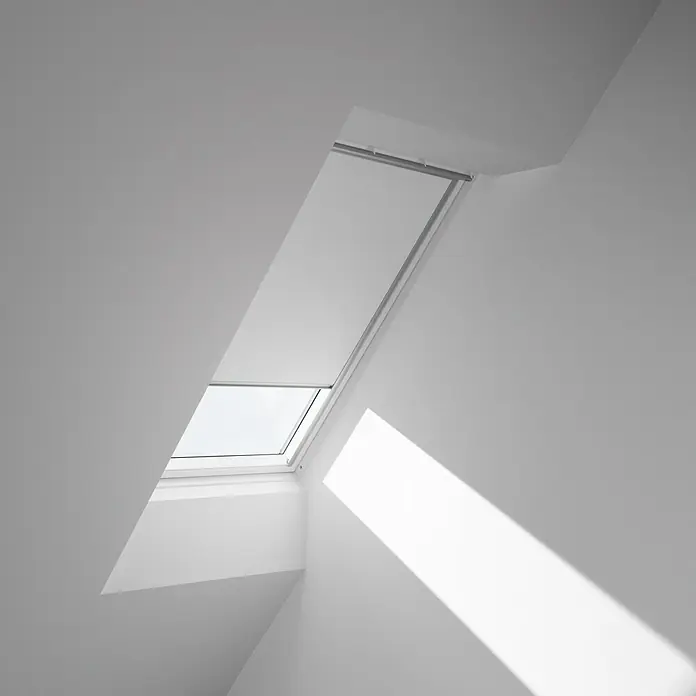 Velux Dachfensterrollo DKL FK06 1025S - Farbe: Weiß - 1025S, Farbe Schiene: Aluminium, Manuell - Das Bild zeigt ein VELUX Dachfenster in einem hellen Raum, das Tageslicht hereinlässt und eine minimalistische Ästhetik betont.