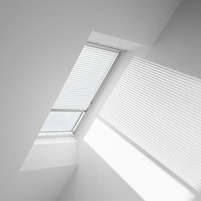 Velux Dachfenster-Jalousie PAL S04 7001S - Farbe: Weiß - 7001S, Farbe Schiene: Aluminium, Manuell - Das Bild zeigt ein Dachfenster mit einem verspannten Plissee-Rollo, das teilweise geöffnet ist und Licht hereinlässt. Die weißen Wände verstärken den modernen Look.