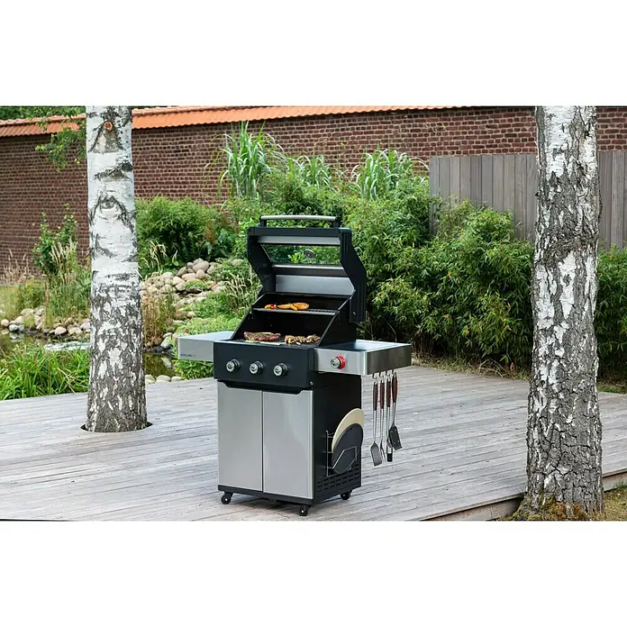 Edelheiss Gasgrill Exzellenz 1.3 - Grillfläche (B x T): 59 x 45,5 cm, 12,6 kW, Anzahl Brenner: 3 Stk. - Ein moderner Edelstahl-Gasgrill mit geöffnetem Deckel, der Steaks und Gemüse zubereitet, steht auf einer hölzernen Terrasse im Garten.
