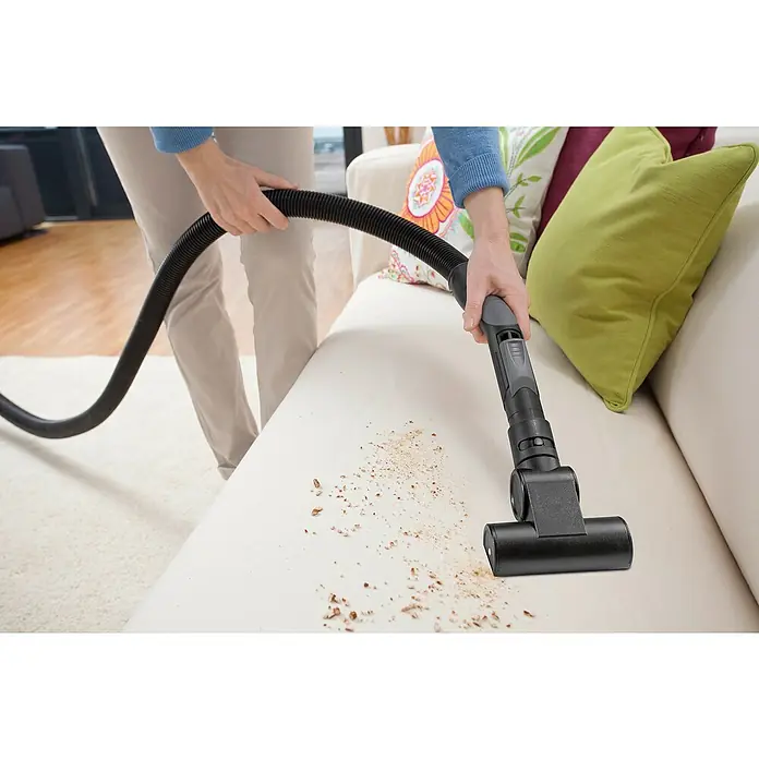 Kärcher Turbopolsterdüse - Passend für: Kärcher Staubsauger VC 2/VC 3 - Staubsauger reinigt ein beiges Sofa mit Krümeln. Der Staubsauger ist schwarz und hat einen grauen Griff. Der Schlauch ist flexibel und schwarz.