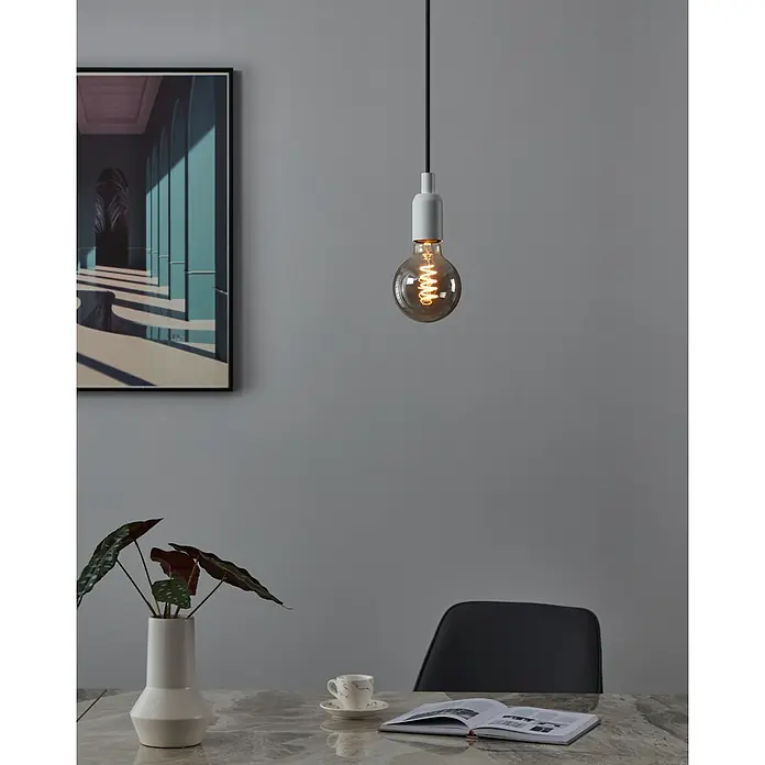 Eglo Bombilla LED - G95, No regulable, Blanco cálido, 100 lm, 4 W - Una lámpara colgante moderna con una bombilla Edison cuelga sobre una mesa con un libro y una taza. Un cuadro cuelga de la pared.