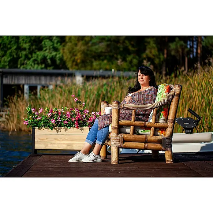 Upyard Pflanzkasten Modernbox tief - 58 x 52 x 48 cm, Holz, Natur - Eine Frau entspannt in einem Bambussessel auf einem Holzsteg am See. Der Sessel bietet Komfort und Stil im Freien.