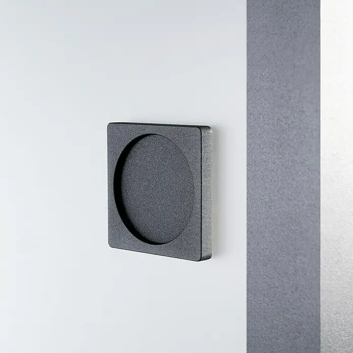 Room Plaza Loft + Mehr Griffmuschel-Set - Schwarz matt, Eckig - Nahaufnahme eines schwarzen, quadratischen Türgriffs mit runder Aussparung an einer weißen Tür, der ein minimalistisches Designelement hervorhebt.