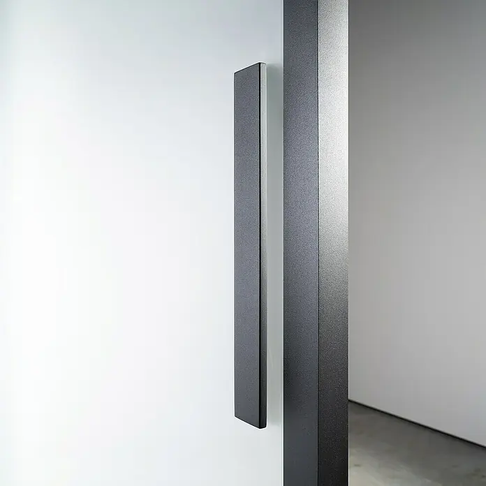 Room Plaza Loft + Mehr Griffstange / Griffleiste - Schwarz matt, 350 x 40 mm, Eckig - Nahaufnahme eines modernen, schwarzen Türgriffs an einer weißen Wand, der das minimalistische Design und die hochwertige Verarbeitung hervorhebt.