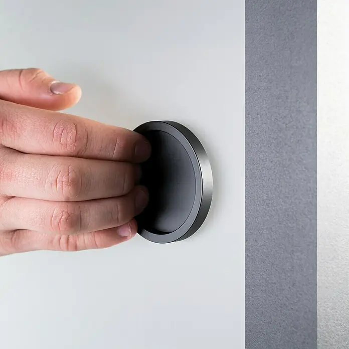 Room Plaza Loft + Mehr Griffmuschel-Set - Schwarz matt, Rund - Nahaufnahme einer Hand, die einen versenkten Griff an einer Schranktür betätigt. Elegantes Design für moderne Möbel.