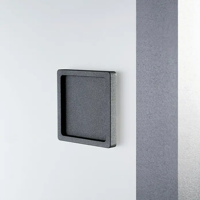 Room Plaza Loft + Mehr Schiebetür-Komplettset - 940 x 2.060 mm, Satiniertes Glas - Nahaufnahme eines quadratischen, schwarzen Briefkastens, der an einer weißen Wand mit einem grauen Streifen auf der rechten Seite montiert ist.