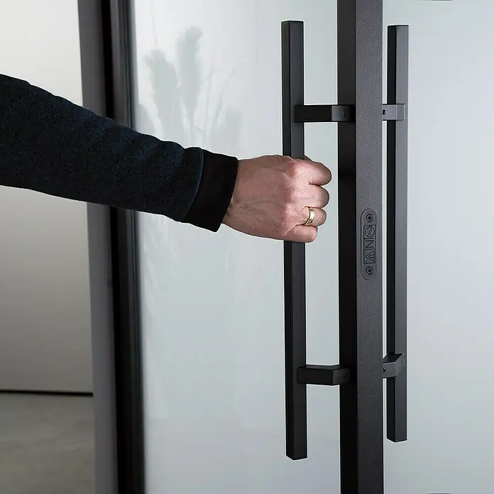 Room Plaza Loft + Mehr Stoßgriff-Set - Schwarz matt, 500 x 40 mm, Eckig - Türgriff im Fokus: Eine Hand öffnet eine moderne Tür mit einem markanten, schwarzen Türgriff.