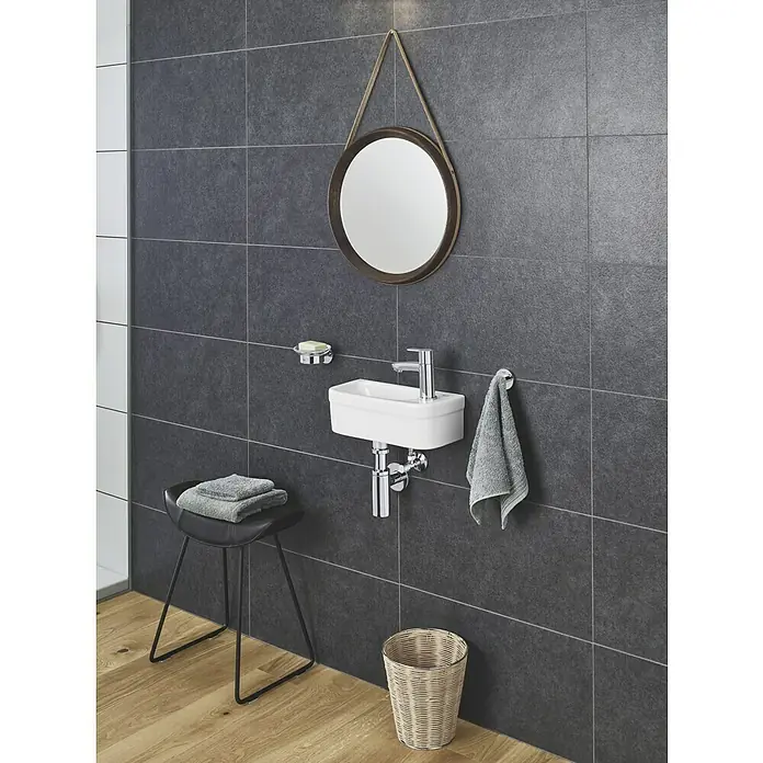 Grohe Eurostyle Cosmopolitan Kaltwasser-Standventil XS-Size - Chrom, Glänzend - Modernes Badezimmer mit einem stilvollen, runden Spiegel, einem weißen Waschbecken und grauen Fliesen für ein minimalistisches Ambiente.