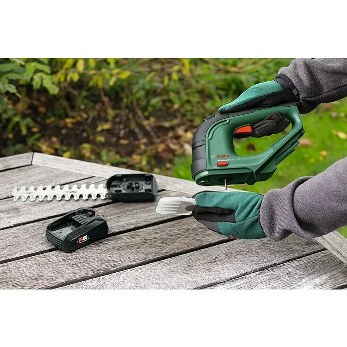 Bosch Power for All 18V Akku-Gras- & Strauchschere AdvancedShear 18V-10 - 18 V, Li-Ionen, 1 Akku, Schwertbreite: 10 cm - Nahaufnahme eines Bosch AdvancedShear 18V Akku-Gartengeräts mit Aufsätzen auf einem Holztisch.