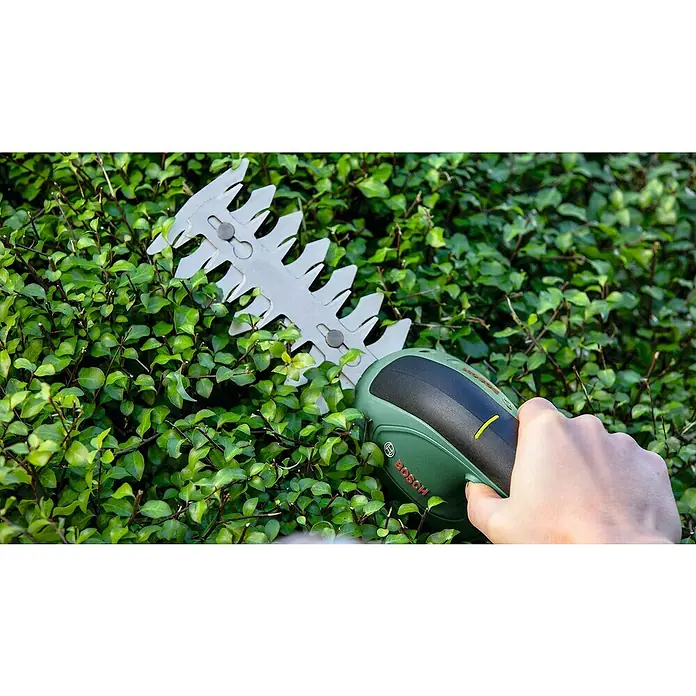 Bosch Akku-Gras- & Strauchschere EasyShear Akku-Gras- & Strauchschere - 3,6 V, Li-Ionen, 1 Akku, Schwertbreite: 8 cm - Nahaufnahme einer Bosch-Akku-Strauchschere beim Schneiden einer grünen Hecke, wobei der Fokus auf dem Werkzeug und seiner Funktion liegt.