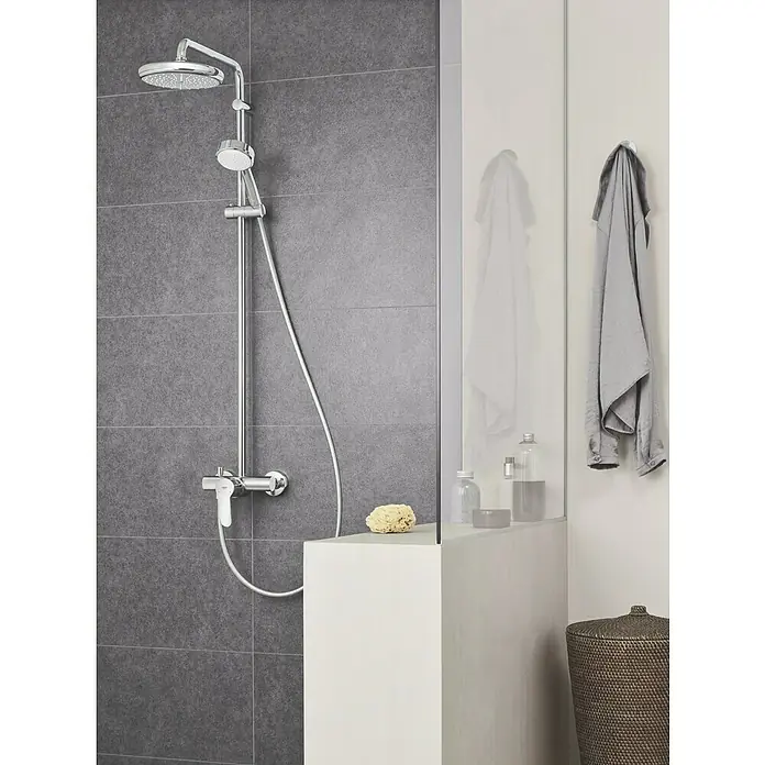 Grohe Tempesta Cosmopolitan Duschsystem - Mit Einhebelmischer, Lochabstand: 101,1 cm, Anzahl Strahlarten: 2 Stk., Chrom - Moderne Dusche mit Chrom-Duschsystem und grauem Fliesenwandhintergrund, ergänzt durch Handtücher und Badutensilien auf einer Ablage.