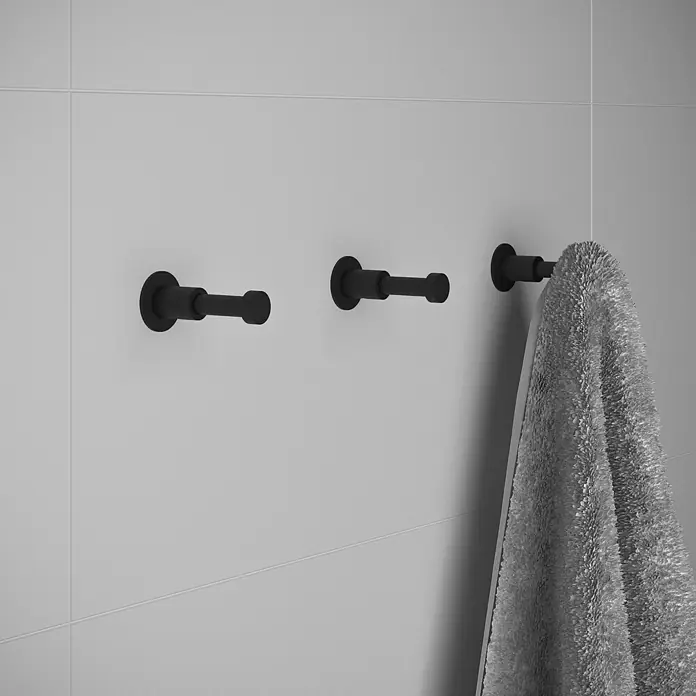 Cosmic Enkel Toallero de gancho - Negro - Tres ganchos de pared negros montados en una pared de azulejos, uno de los cuales tiene una toalla gris colgando.