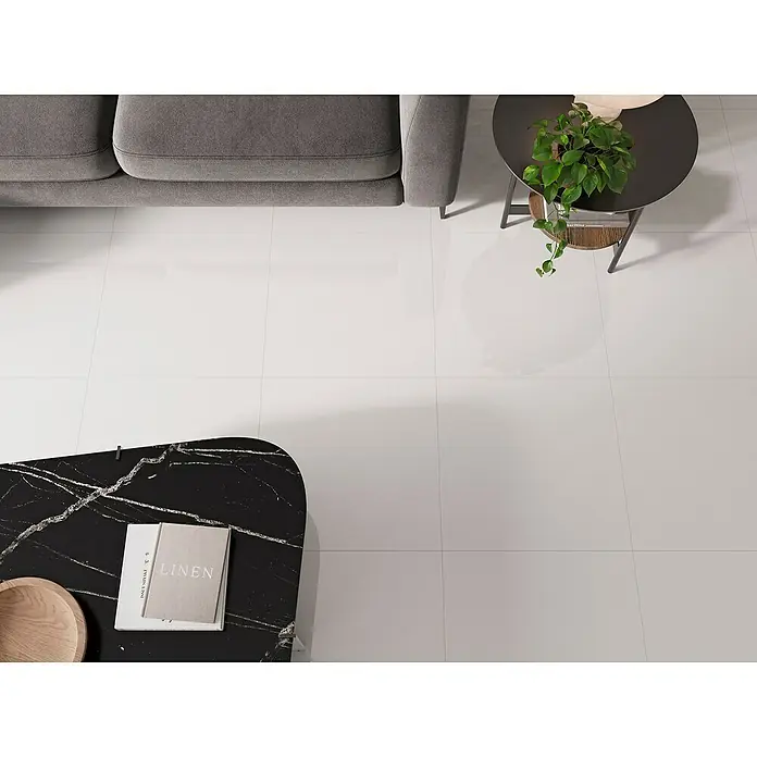 Feinsteinzeugfliese Super White - 59,8 x 59,8 cm, Weiß, Glänzend - Ein stilvolles Wohnzimmer mit glänzenden weißen Fliesen, einer Couch und einem Tisch mit Buch und Pflanze. Die weißen Fliesen sorgen für ein helles Ambiente.