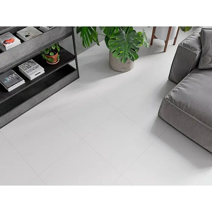 Feinsteinzeugfliese Super White - 59,8 x 59,8 cm, Weiß, Matt - Nahaufnahme eines Wohnzimmers mit einem grauen Sofa, einem Bücherregal mit Büchern und einer Zimmerpflanze auf einem weißen Fliesenboden.