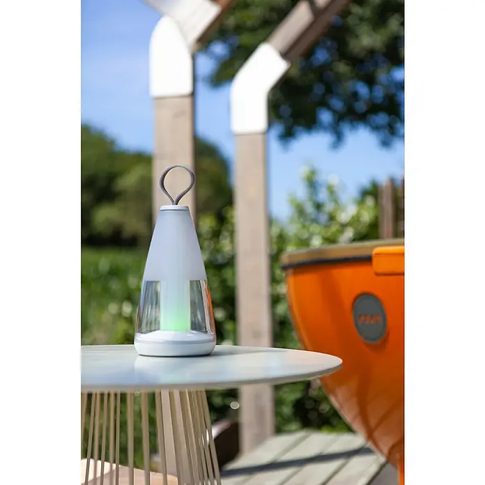 Lutec Akku-Tischleuchte PEPPER - 3 W, L x B x H: 12 x 12 x 29 cm, Weiß, RGBW - Eine moderne, kabellose Tischleuchte mit grünem Lichtakzent steht auf einem Tisch im Freien.