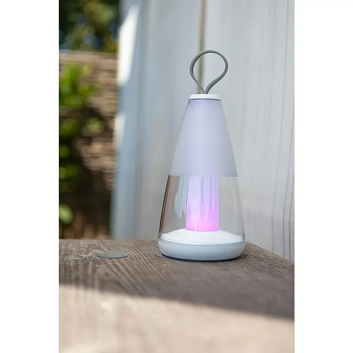 Lutec Akku-Tischleuchte PEPPER - 3 W, L x B x H: 12 x 12 x 29 cm, Weiß, RGBW - Nahaufnahme einer tragbaren LED-Lampe mit Farbwechsel, die auf einem Holztisch steht und ein warmes, farbenfrohes Licht ausstrahlt.