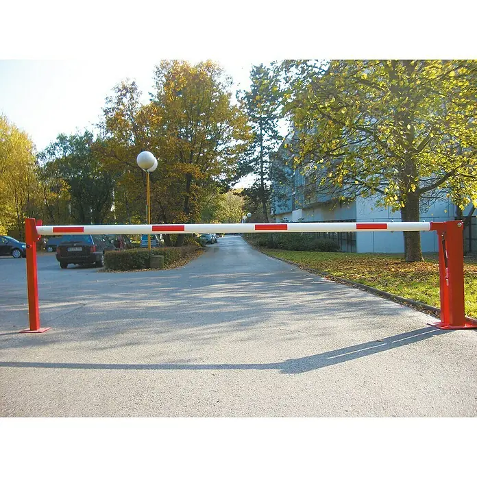 Schake Handschranke - Mit Auflagepfosten, Art Schloss: Dreikantverriegelung & Profilzylinderschloss, Länge: 3.180 mm - Roter und weißer Schrankenbaum, der eine Zufahrt blockiert, mit herbstlichen Bäumen und einem Gebäude im Hintergrund.