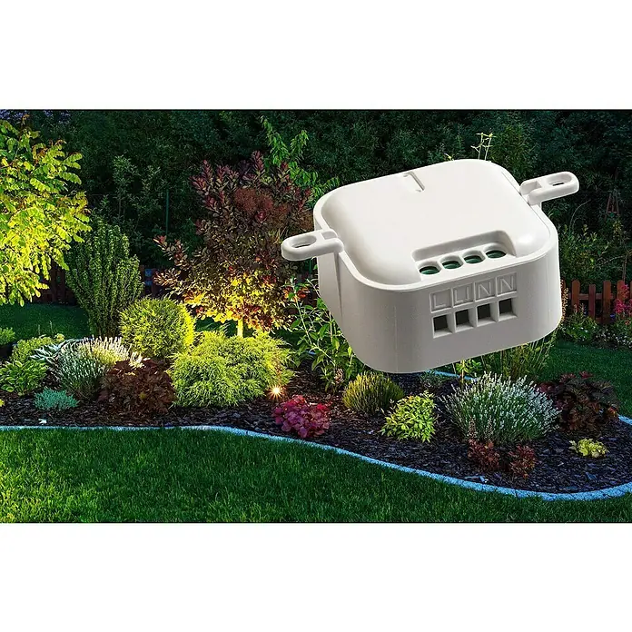 Intertechno Funk-Einbauschalter CMR-2000 - Max. Anschlussleistung: 2.000 W - Nahaufnahme einer weißen Verteilerdose mit Klemmen in einem Garten mit Beet und Pflanzen.
