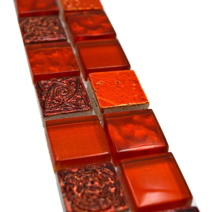 Fliesenbordüre YBO CB30 - 30 x 4,8 cm, Mix Rot, Glänzend - Nahaufnahme von orangefarbenen Glasmosaikfliesen mit verschiedenen Mustern und Texturen, die ein dekoratives Element für Innenräume darstellen.