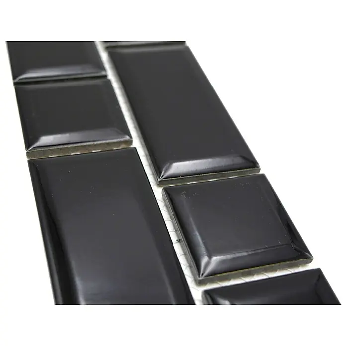 Fliesenbordüre Uni YBO M02BM - 4,5 x 29,4 cm, Schwarz, Glänzend - Nahaufnahme von glänzenden, schwarzen Metrofliesen mit abgerundeten Kanten, die auf einem weißen Untergrund liegen.