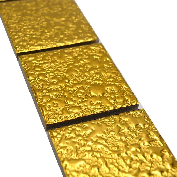 Fliesenbordüre Gehämmert YBO GO484 - 4,8 x 30,6 cm, Gold, Glänzend - Nahaufnahme von drei goldenen Mosaikfliesen mit unebener Oberfläche, die nebeneinander auf einer weißen Fläche liegen.