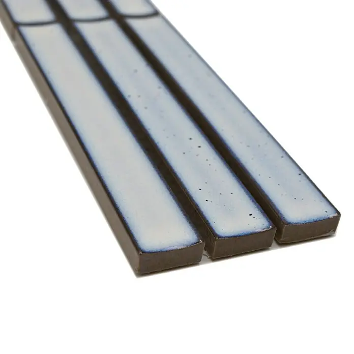 Fliesenbordüre YBO CS66 - 6,9 x 29,6 cm, Weß, Glänzend - Nahaufnahme von drei bläulich-weißen Keramikfliesen mit dunklen Rändern, die auf einer weißen Oberfläche liegen.