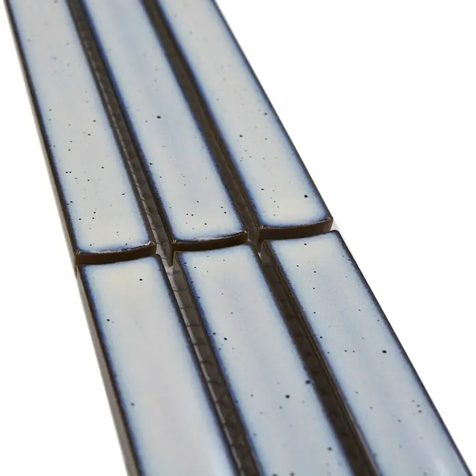 Fliesenbordüre YBO CS66 - 6,9 x 29,6 cm, Weß, Glänzend - Detailaufnahme von länglichen, hellblauen Keramikfliesen mit dunklem Rand und feinen Sprenkeln, die nebeneinander liegen.
