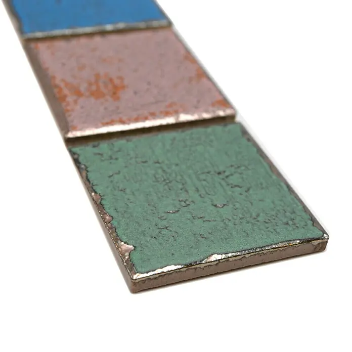 Fliesenbordüre Orient Color YBO CDCUBIS - 5 x 31,6 cm, Bunt, Matt - Nahaufnahme von drei quadratischen, farbig emaillierten Metallplättchen in Blau, Rosa und Grün, die einen charmanten, rustikalen Look zeigen.