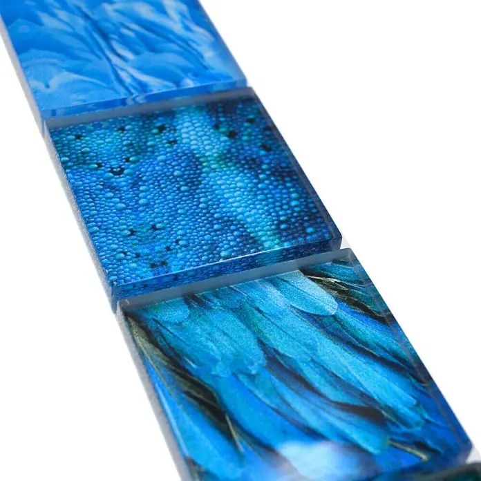 Fliesenbordüre Wildlife YBO WL78 - 29,8 x 4,8 cm, Blau, Glänzend - Nahaufnahme von drei quadratischen Glasfliesen mit blauen Farbverläufen und verschiedenen Mustern.