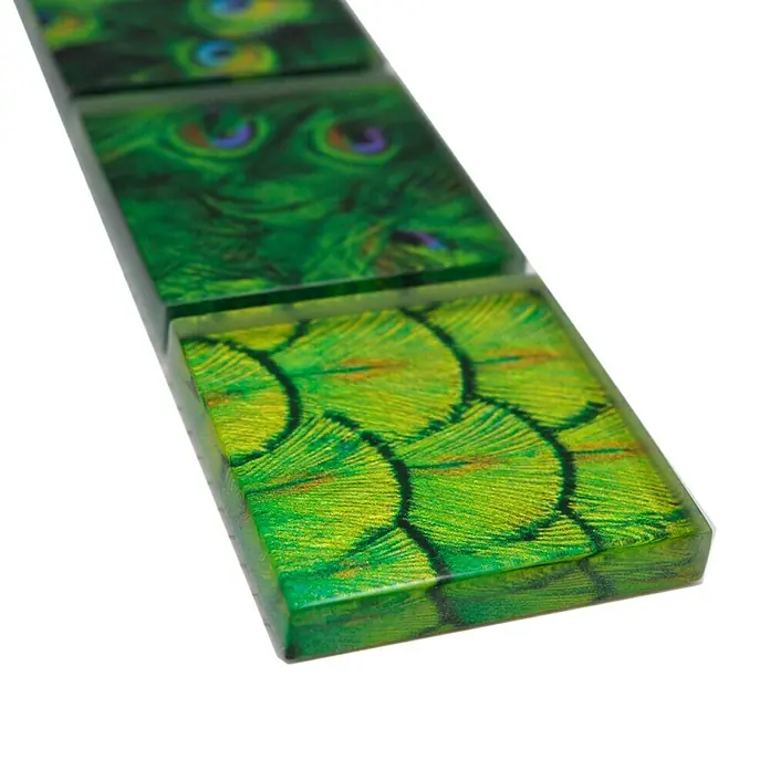 Fliesenbordüre Wildlife YBO WL88 - 29,8 x 4,8 cm, Grün, Glänzend - Das Bild zeigt dekorative Glasfliesen mit grünem Pfauenfederdesign. Die Fliesen haben eine glänzende Oberfläche und sind quadratisch geformt.