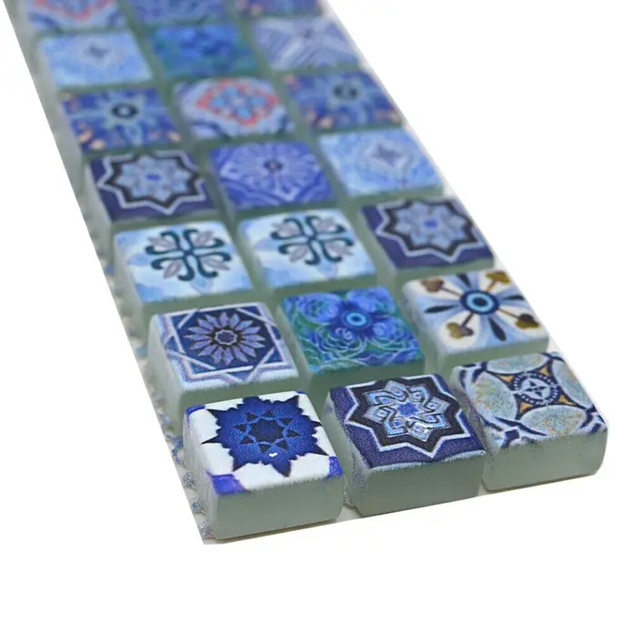 Fliesenbordüre YBO RB33 - 30 x 4,8 cm, Blau, Glänzend - Nahaufnahme eines Musters aus quadratischen blauen Mosaikfliesen mit unterschiedlichen Designs. Die Fliesen sind auf einem Blatt angeordnet und haben eine glatte Oberfläche.