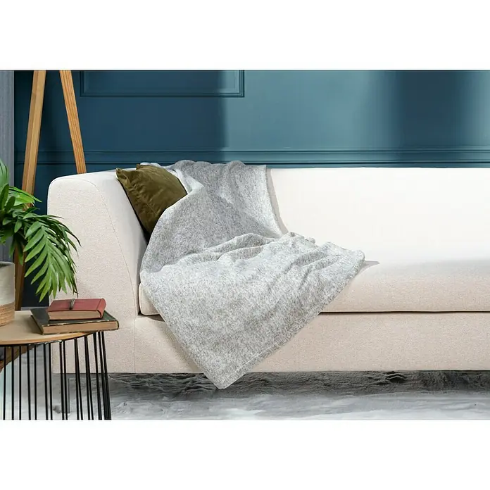 Decke Melange - Light Beige, 170 x 130 cm, 100 % Polyester - Eine helle Couch mit einer weichen, grauen Strickdecke und einem grünen Kissen darauf, die eine gemütliche und einladende Atmosphäre schafft.