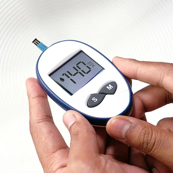 Energizer Knopfzelle - CR2032, 3 V, 6 Stk. - Blutzuckermessgerät in der Hand, das einen Wert von 140 mg/dL anzeigt. Das Gerät ist weiß mit blauem Rand und hat eine Teststreifen-Einführung.