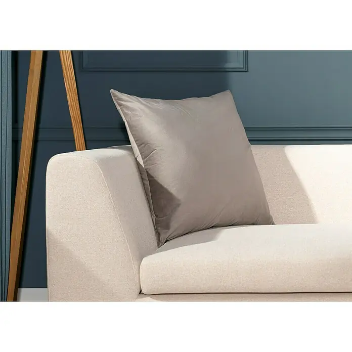 Kissen Finja - Driftwood, 60 x 60 cm, 100 % Polyester - Ein graues Samtkissen liegt auf einem hellen Sofa vor einer dunkelblauen Wand. Das Kissen ist quadratisch und wirkt weich und einladend.