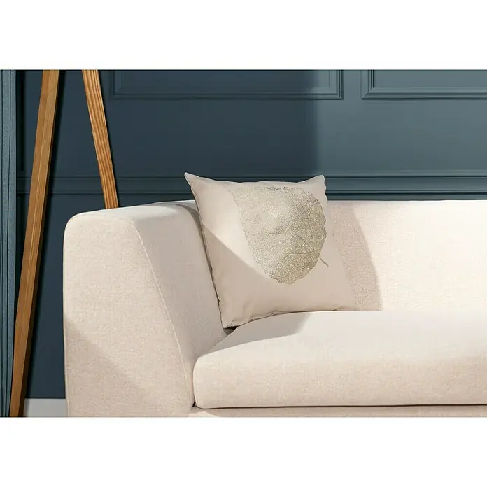 Kissen Troy - Crystal Grey Champagne, 45 x 45 cm, 100 % Baumwolle - Nahaufnahme eines cremefarbenen Sofas mit einem dekorativen Kissen, das ein Blattmotiv trägt. Die sanfte Farbpalette strahlt Ruhe aus.