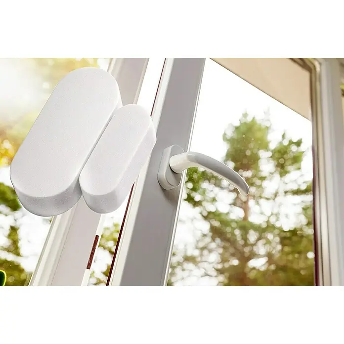 Intertechno Funksender Magnet ITM-200 - 46 x 32 x 12 mm - Nahaufnahme eines weißen Fensterkontakts an einem Fenster, der die Sicherheit des Zuhauses erhöht und Einblicke in das Äußere ermöglicht.