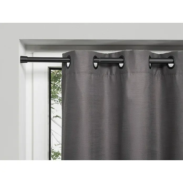 Spannstange Stretch - Schwarz, Auszugslänge: 80 cm - 130 cm - Grauer Verdunkelungsvorhang mit Metallösen hängt an einer schwarzen Gardinenstange vor einem Fenster.