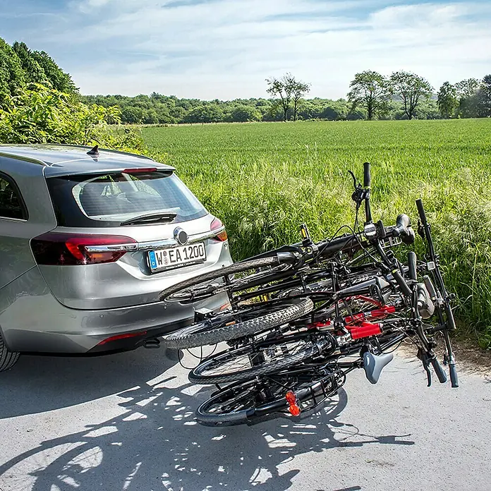 Eufab Fahrradträger Amber IV - Geeignet für: 4 Fahrräder, Passend für: Fahrzeuge mit Anhängerkupplung - Ein silberner Kombi mit einem Fahrradträger, beladen mit mehreren Fahrrädern auf einer Landstraße, umgeben von Feldern.