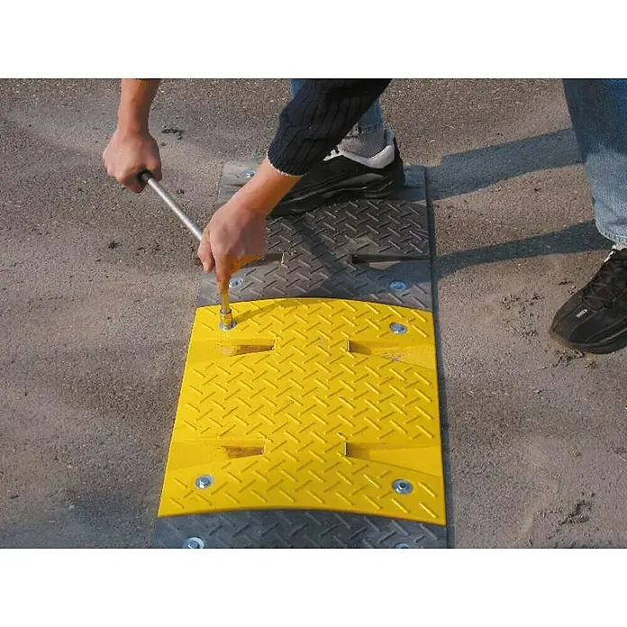 Schake Bodenschwelle Mittelstück NOX - L x B: 500 x 430 mm, Höhe: 60 mm, Farbe: Gelb, Kunststoff - Person befestigt mit Schraubenschlüssel einen gelben Geschwindigkeitsbegrenzer auf einer grauen Unterlage.
