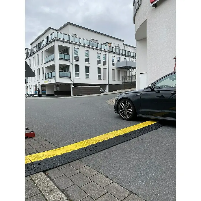 Schake Bodenschwelle Mittelstück NOX - L x B: 500 x 430 mm, Höhe: 60 mm, Farbe: Gelb, Kunststoff - Geschwindigkeitsbegrenzer aus Gummi mit gelben und schwarzen Elementen auf einer städtischen Straße vor einem Auto.