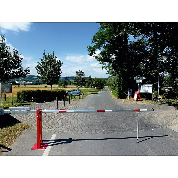 Schake Wegeschranke - Mit Pendelstütze, Art Schloss: Profilzylinderschloss, Länge: 4.900 mm - Roter und silberner Schrankenbaum, der den Weg versperrt, mit Bäumen und blauem Himmel im Hintergrund.