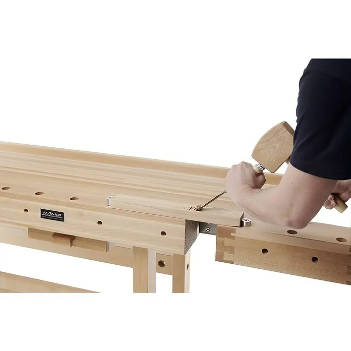 Ramia Hobelbank Premium Monster - L x B: 2.120 x 790 mm, Arbeitshöhe: 870 mm, Holz - Ansicht einer RAMIA Werkbank aus Holz mit einer Person, die einen Meißel und einen Hammer benutzt, um an einem Holzstück zu arbeiten.