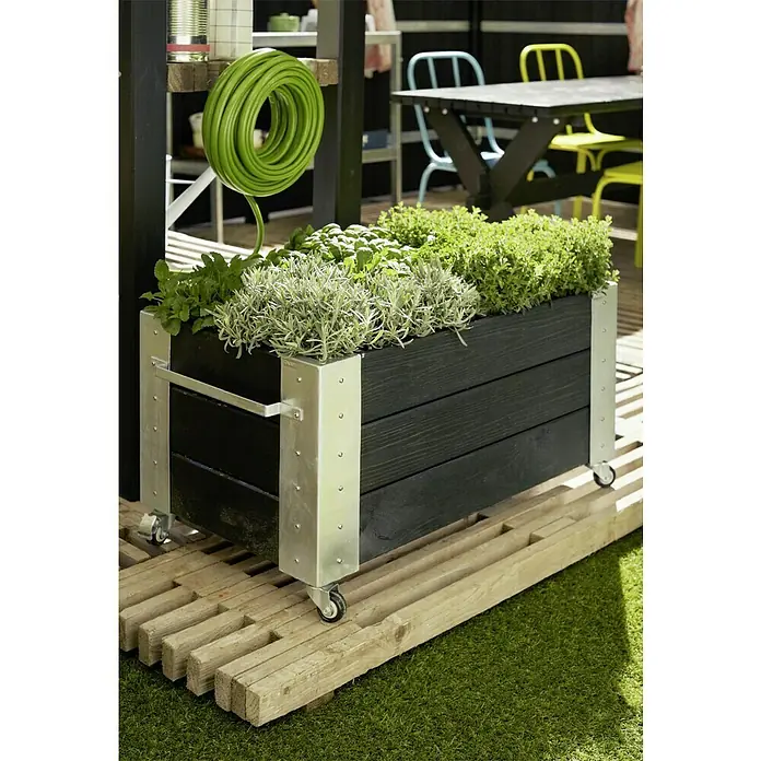Plus Pflanzkübel eckig Cubic - 87 x 50 x 45 cm, Schwarz, Kiefer - Ein Pflanzkasten aus Holz mit Rollen und Metallverstärkungen, bepflanzt mit verschiedenen Kräutern, steht auf einem Holzrost.