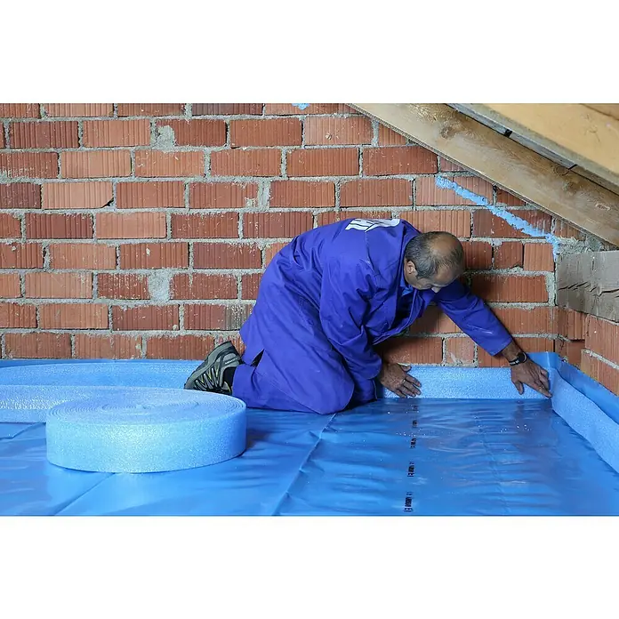 Bachl Dachbodenelement - Stärke: 120 mm, L x B: 1.000 x 500 mm - Ein Mann verlegt blaue Randdämmstreifen auf einer blauen Folie vor einer Ziegelwand, um den Boden zu isolieren und vor Feuchtigkeit zu schützen.